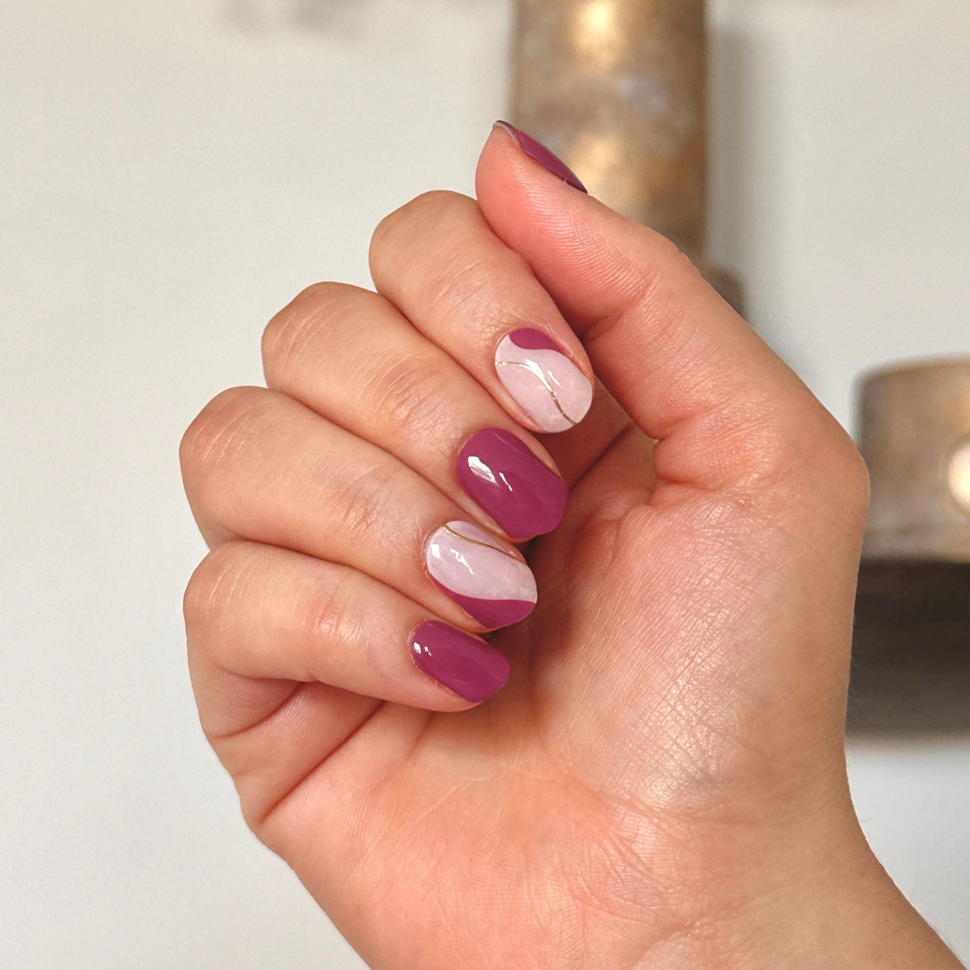 Gel nagel stickers met verschillende nagels, de meeste nagels zijn een effen paarse berry kleur en andere nagel is een combinatie van een off white kleur met dezelfde berry kleur en een gouden lijn in swirl vorm