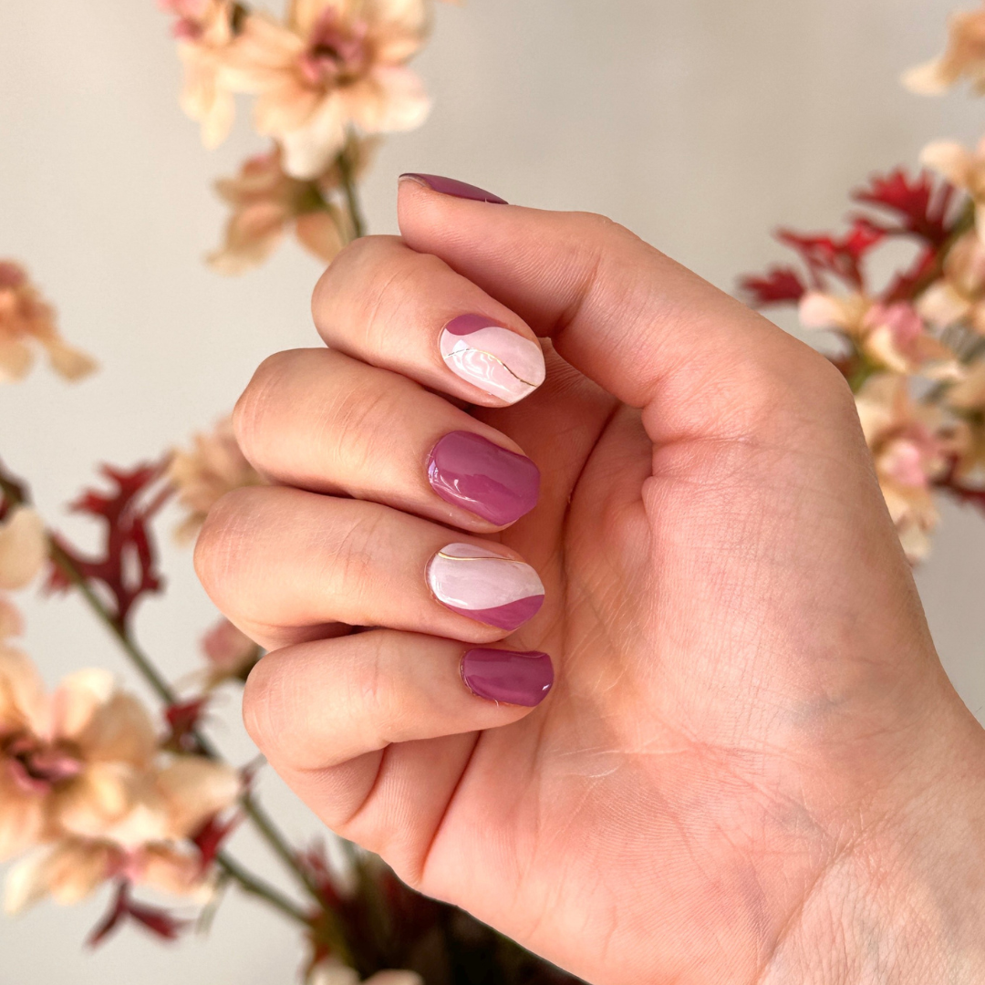Gellakstickers met verschillende nagels, de meeste nagels zijn een effen paarse berry kleur en andere nagel is een combinatie van een off white kleur met dezelfde berry kleur en een gouden lijn in swirl vorm