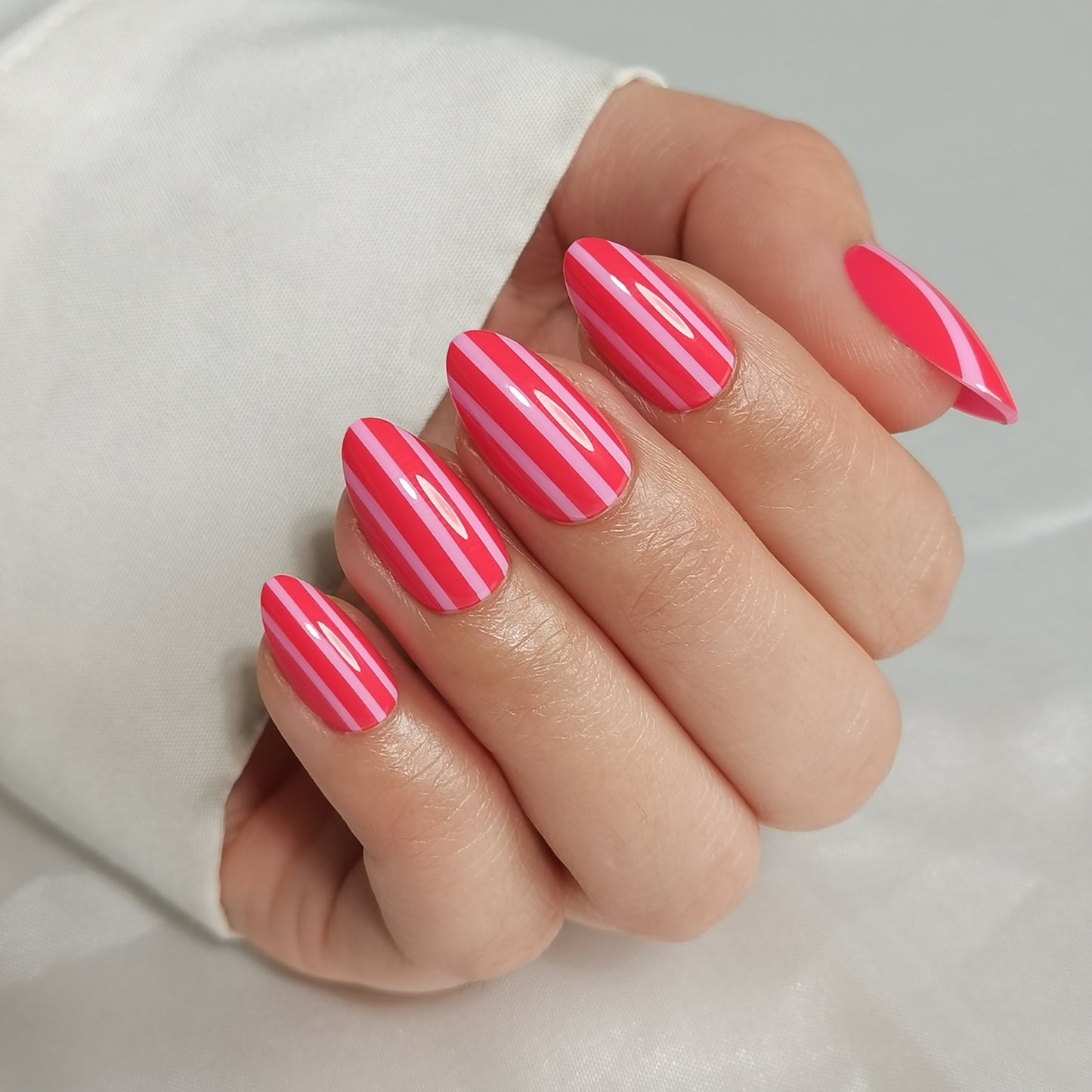 Roze gestreepte soft gel press-on nagels in almond vorm met neonroze en lichtroze verticale strepen.